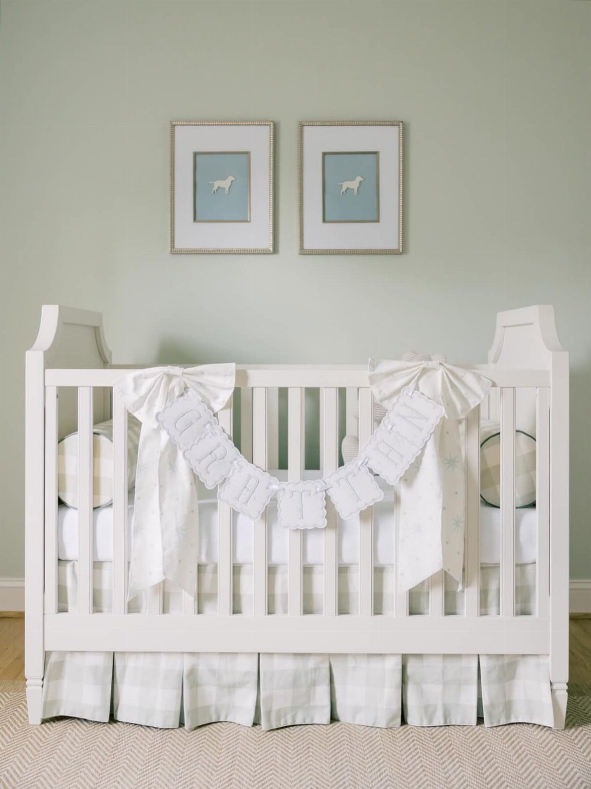 White baby crib with decorative bows and dog portraits on a pale green wall