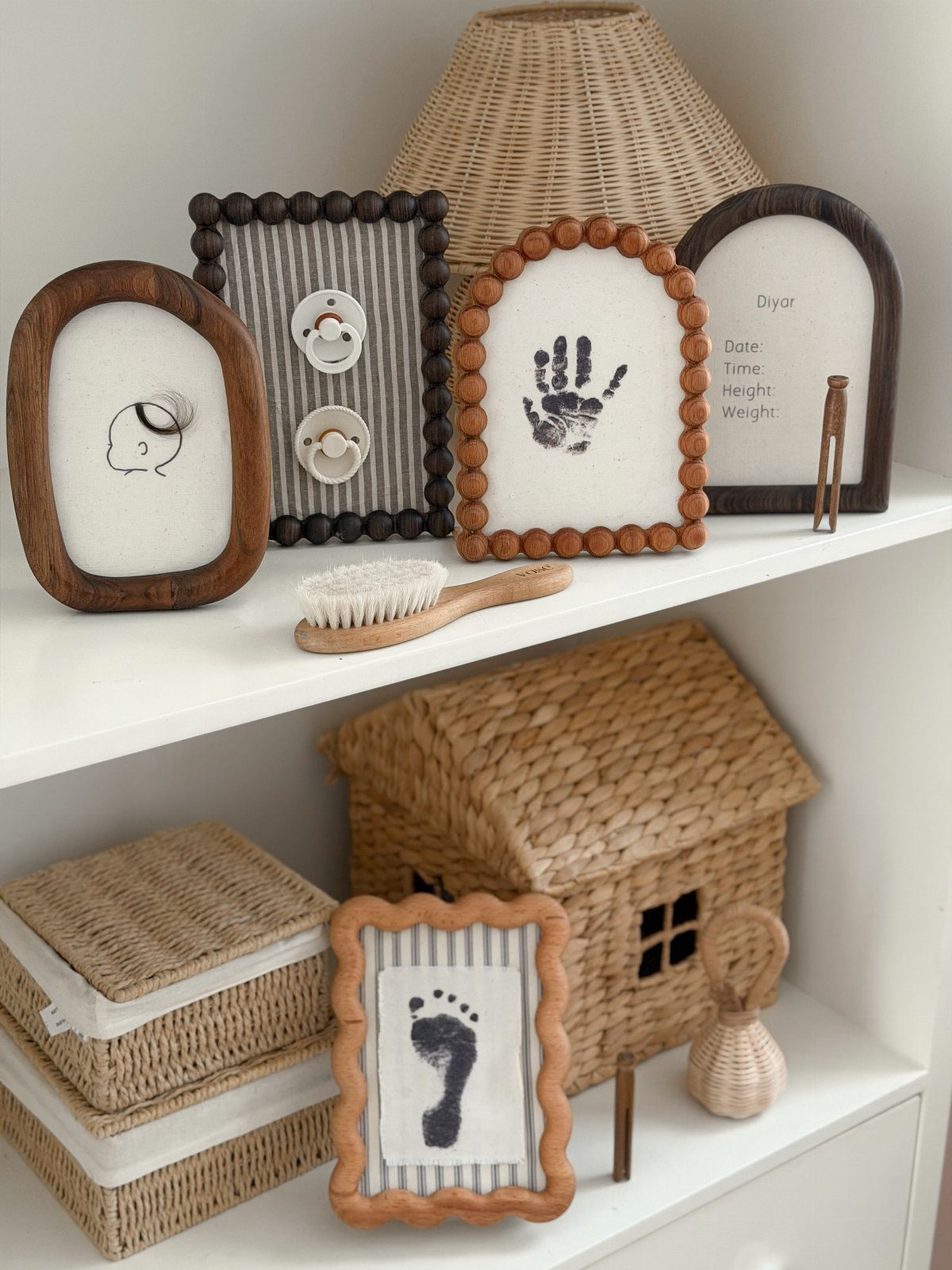 Framed baby handprints and footprints displayed on a white shelf with woven decor.