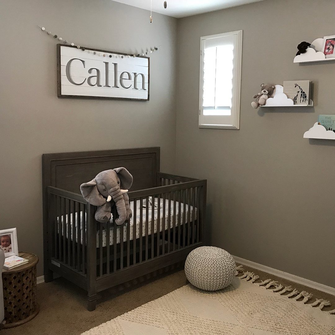 Grey nursery with a wooden crib, plush elephant, and neutral decor.