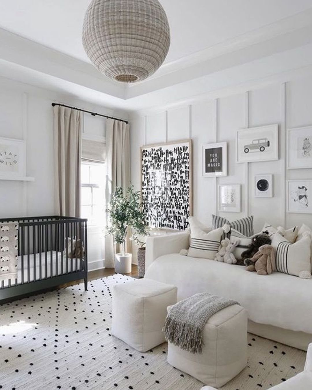 Neutral nursery with black crib, white sofa, and white paneled walls.