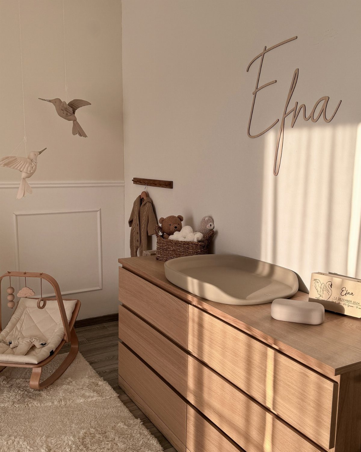 Light wood dresser and baby rocker in a minimalist neutral Scandinavian nursery room