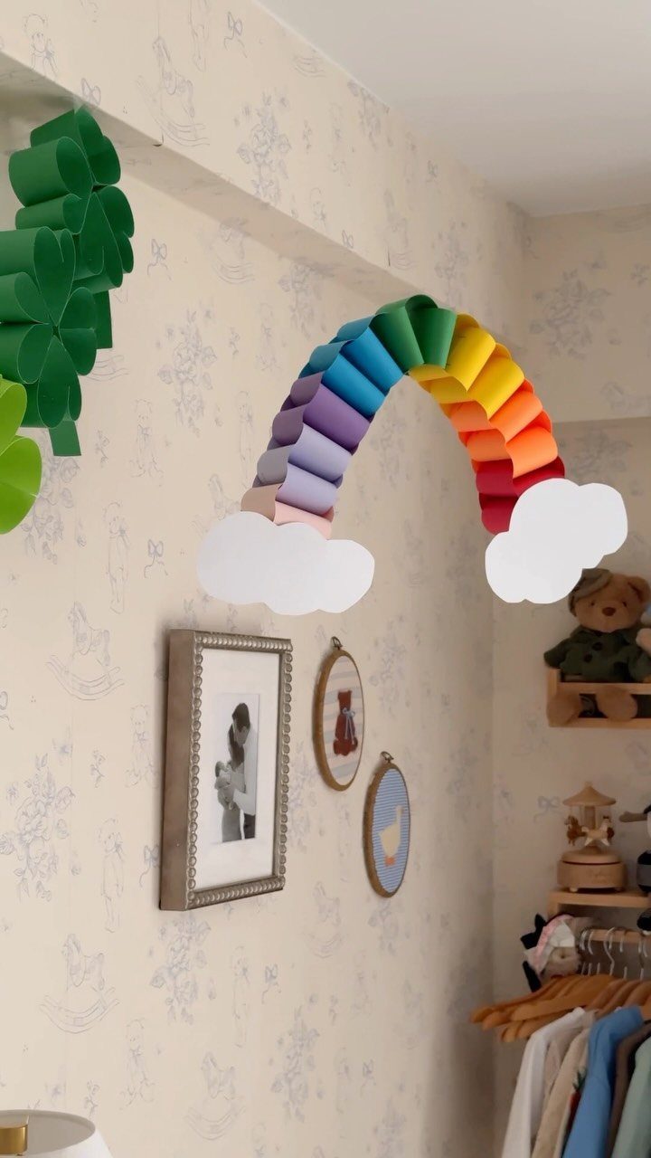 Colorful paper rainbow with white clouds on a patterned nursery wall with frames.