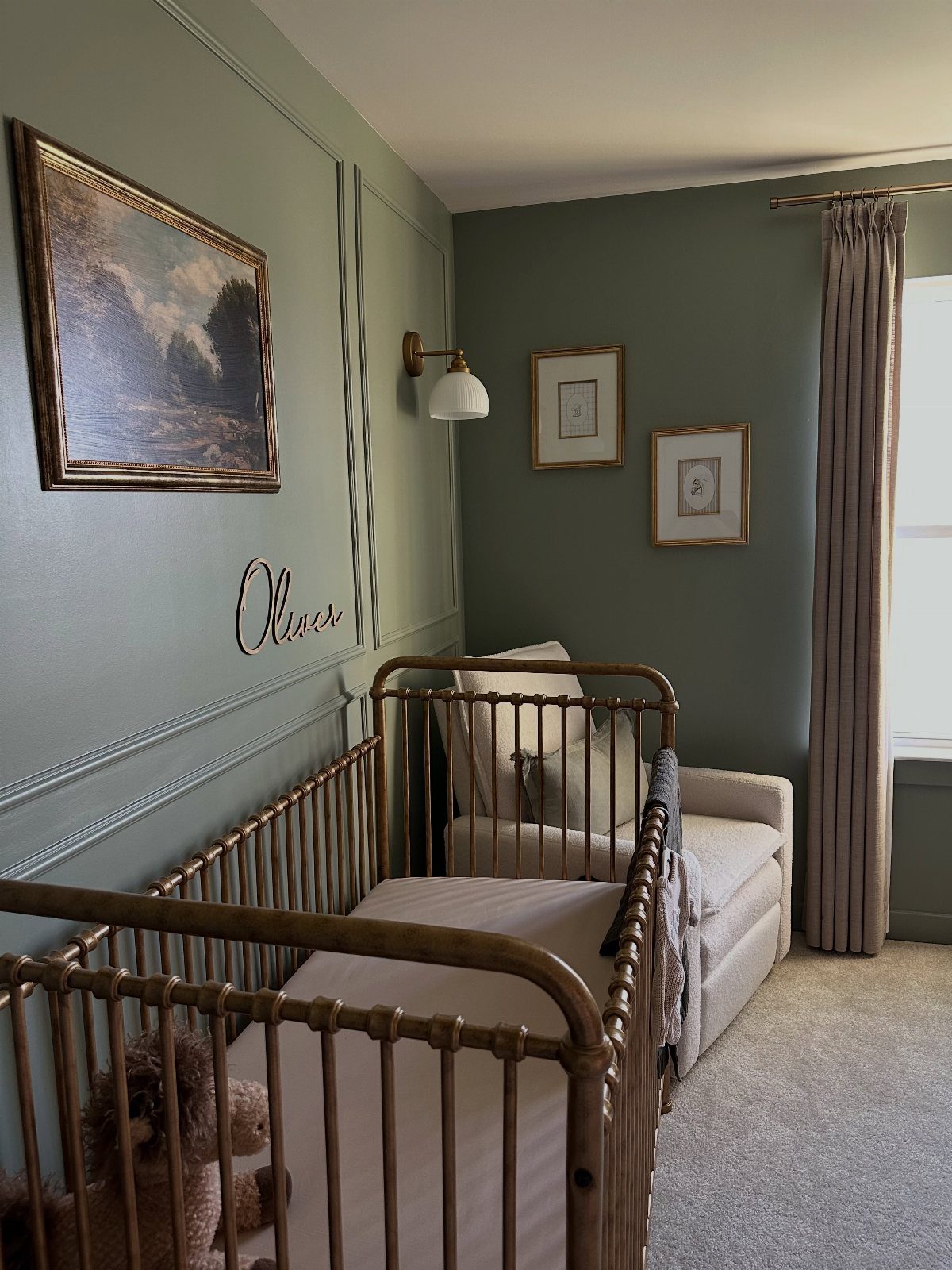 Sage green nursery with a gold metal crib and neutral beige armchair.