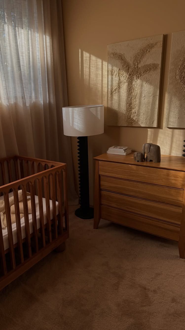 Wooden crib and dresser in a neutral nursery with beige walls and art.