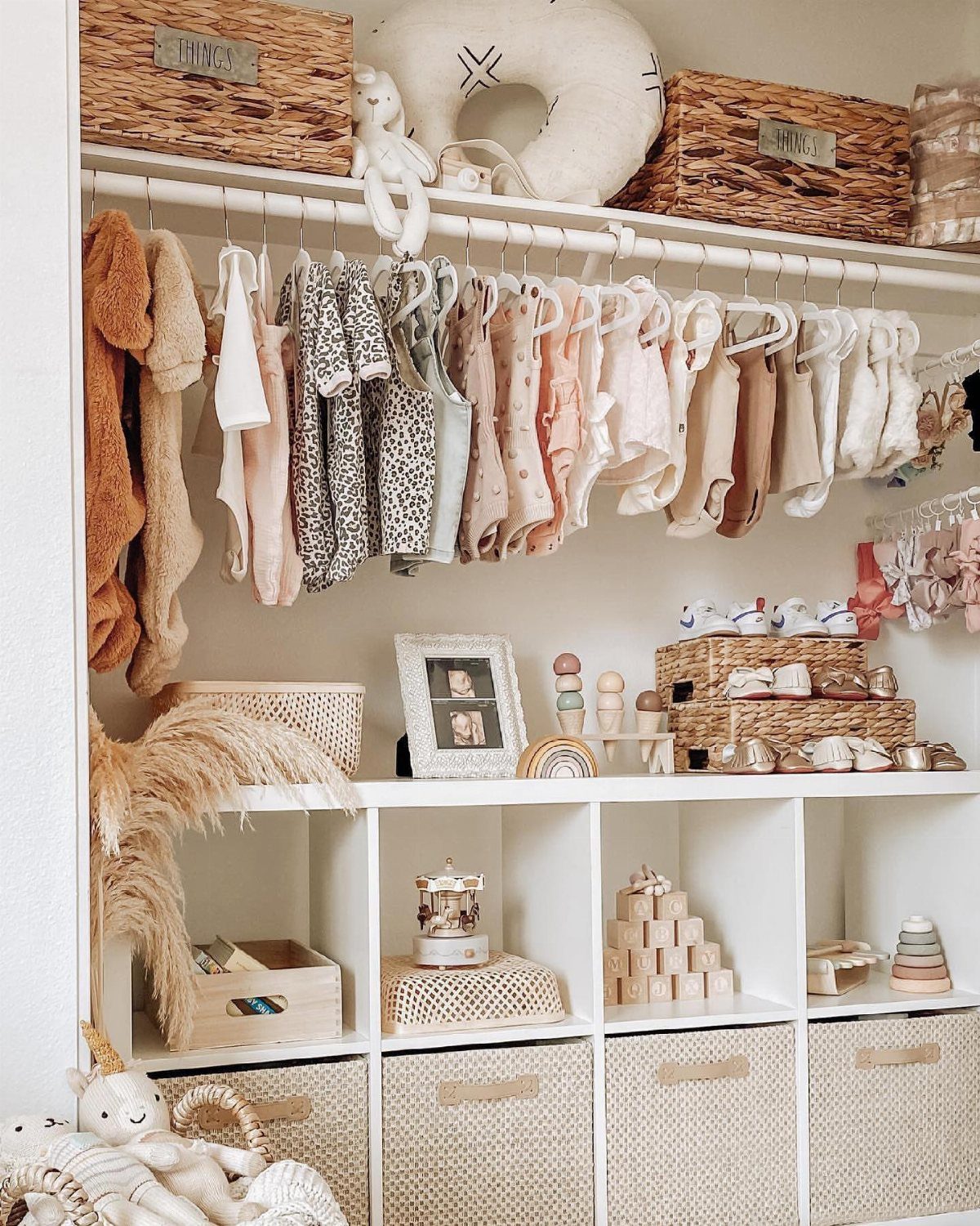 Closet nursery nook with hanging baby clothes and white cubby storage with baskets.