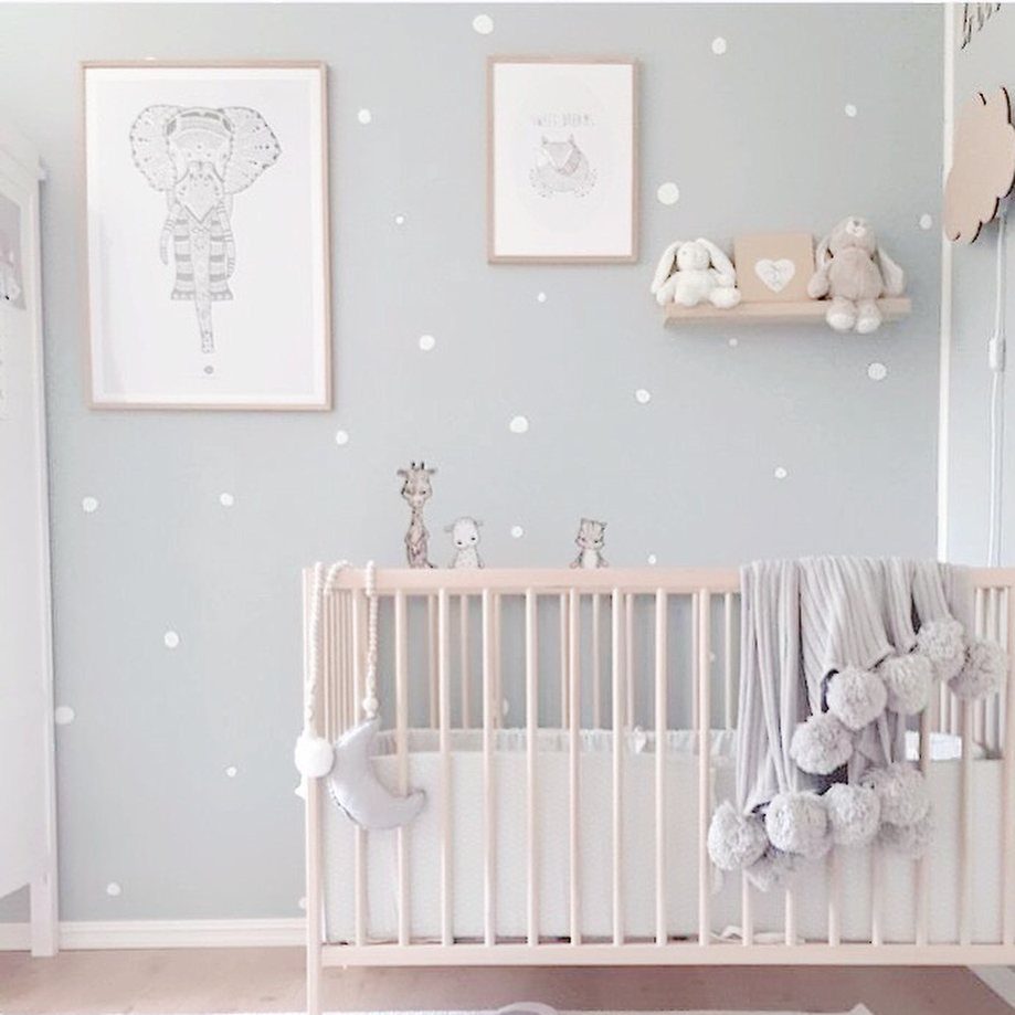 Wooden crib in a nursery with light blue polka dot walls and framed art.