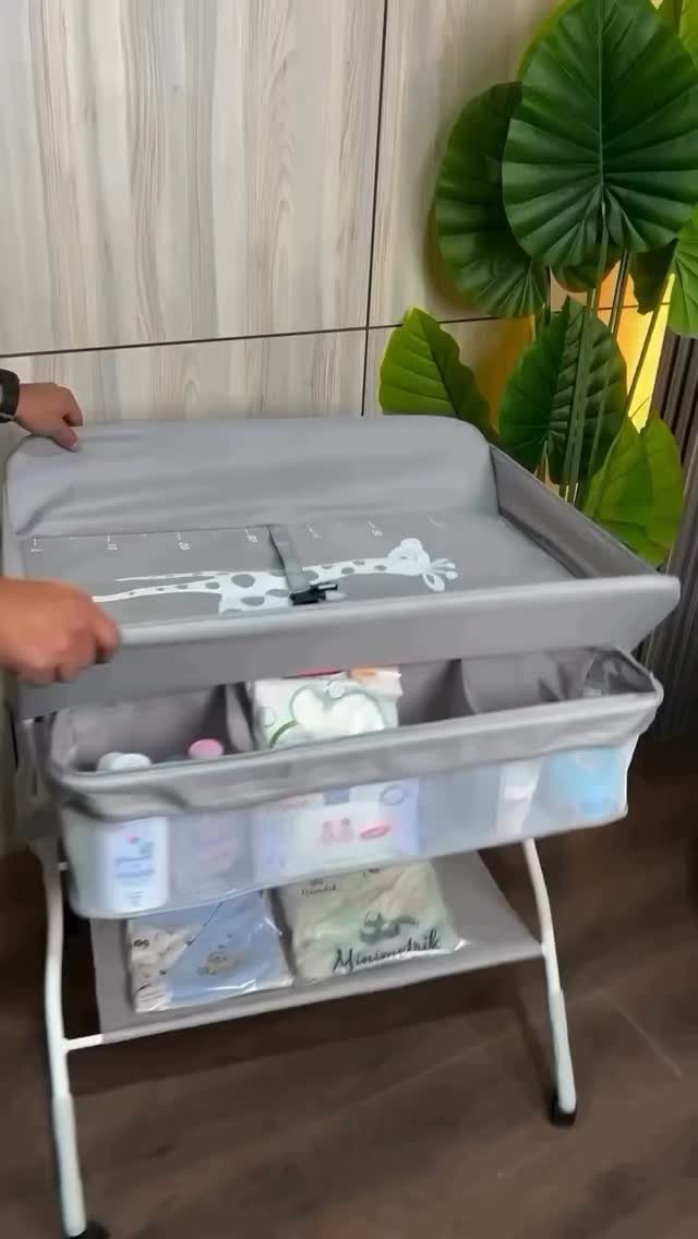 Grey portable baby changing station with storage bins on a wheeled white frame.