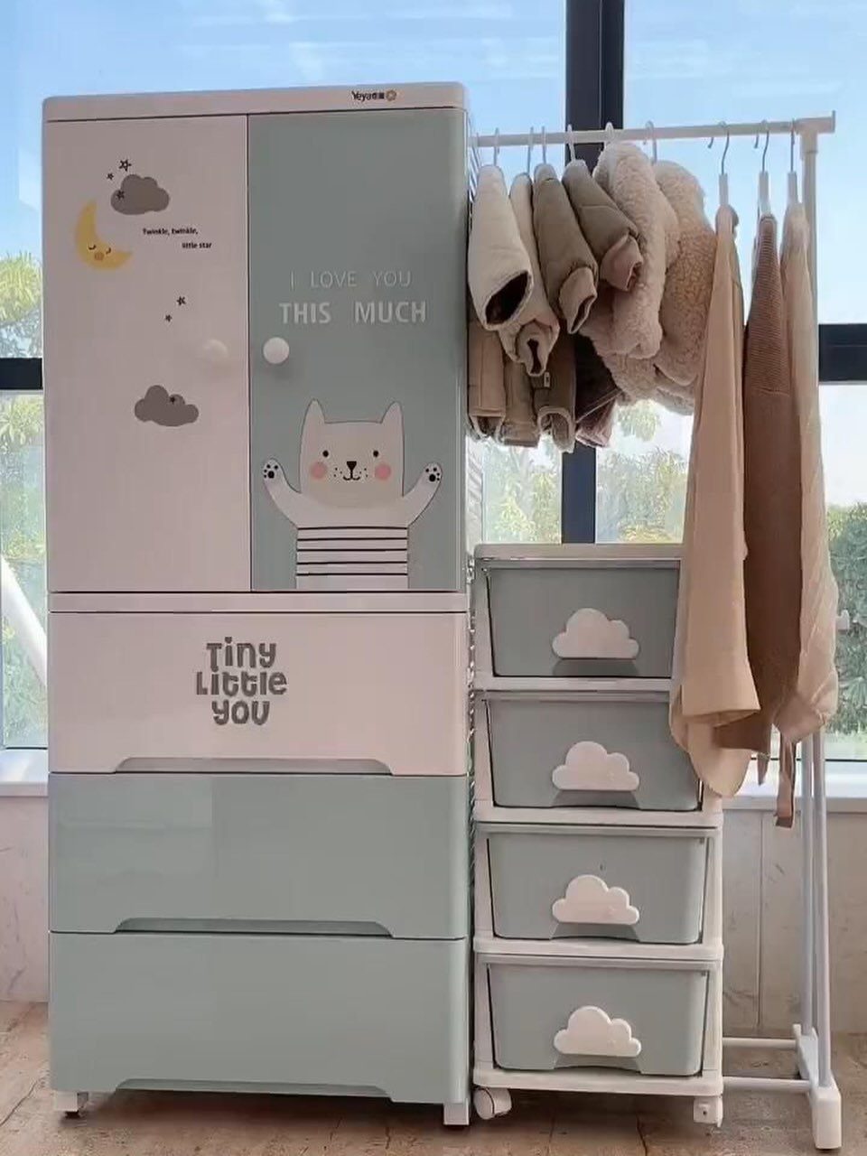 Baby wardrobe and drawer units in mint green and white with hanging clothes.