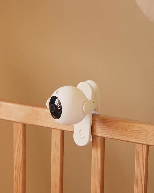 White baby monitor camera mounted on the wooden rail of a baby crib.