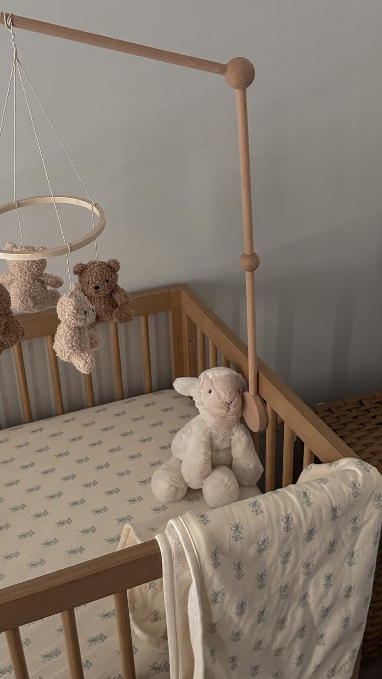 Wooden baby crib with patterned white crib sheets and a plush lamb toy.