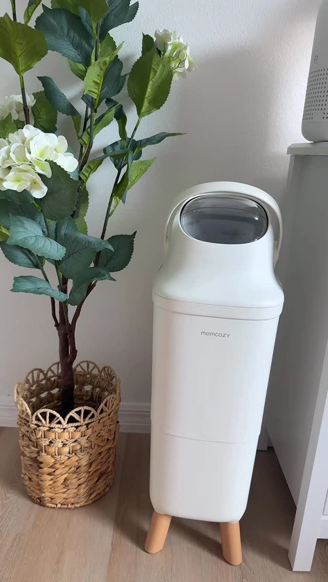 White modern diaper pail with wooden legs next to a potted plant.