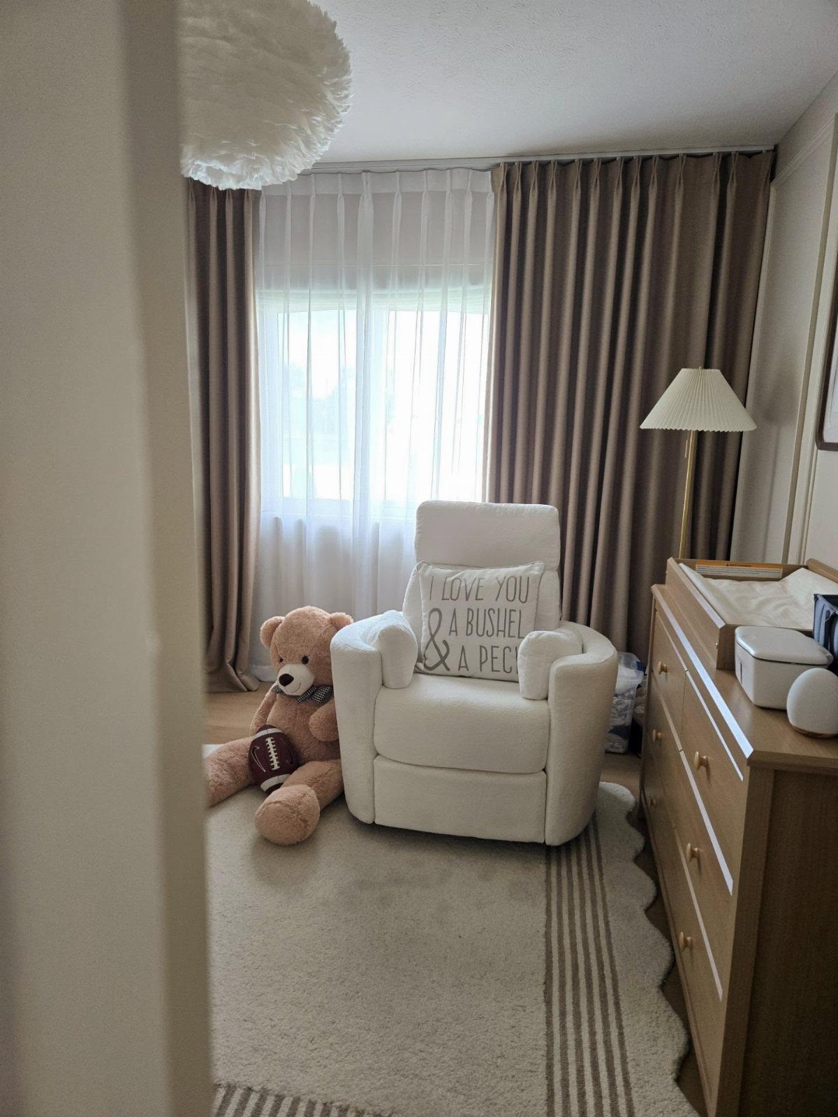 White glider chair and teddy bear in a nursery with brown blackout curtains.
