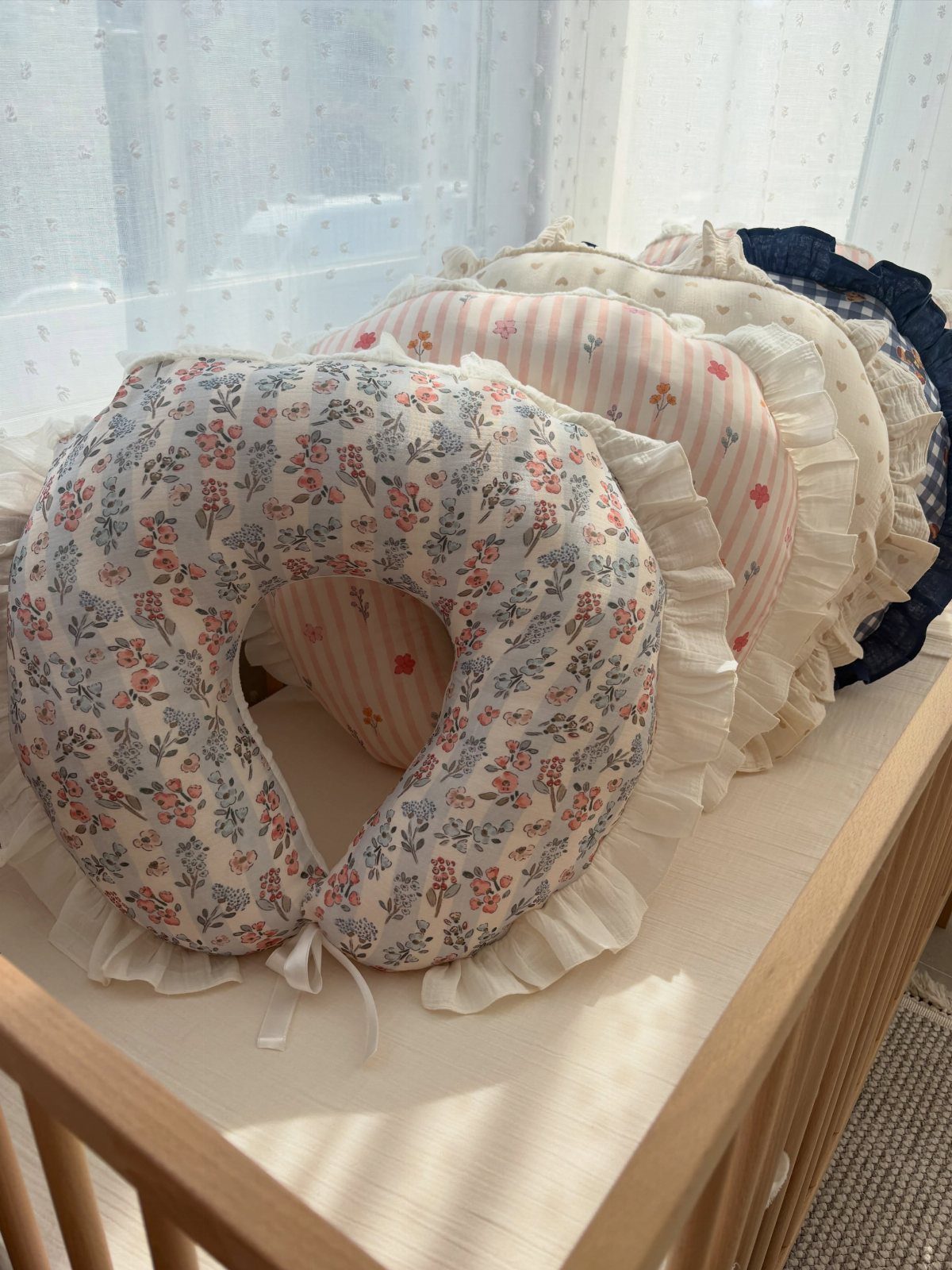 Nursing pillows with floral and striped patterns resting on a wooden baby crib