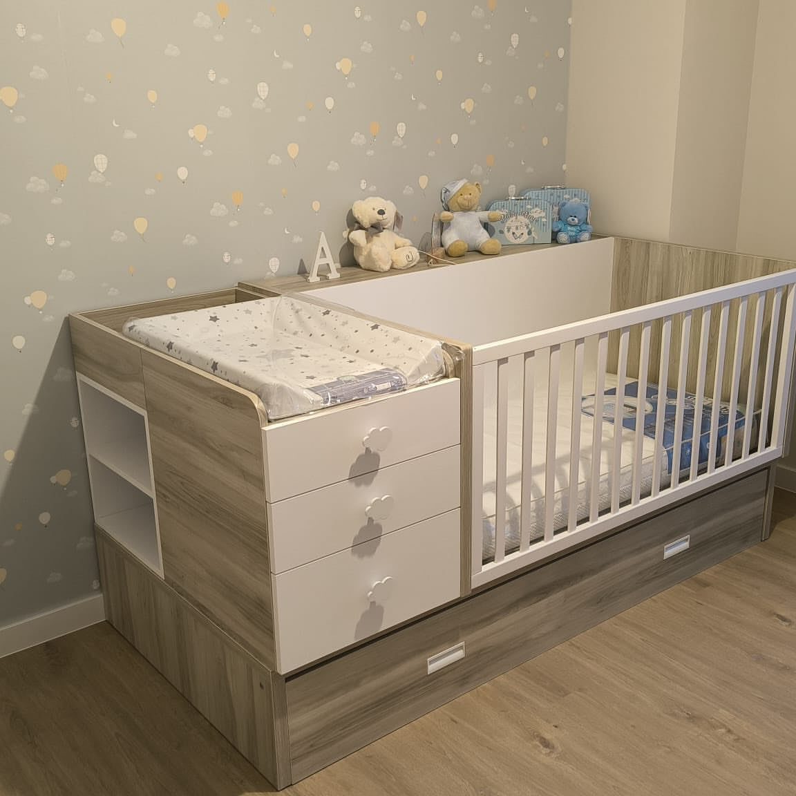Light wood crib with integrated changing table and drawers in a grey nursery.