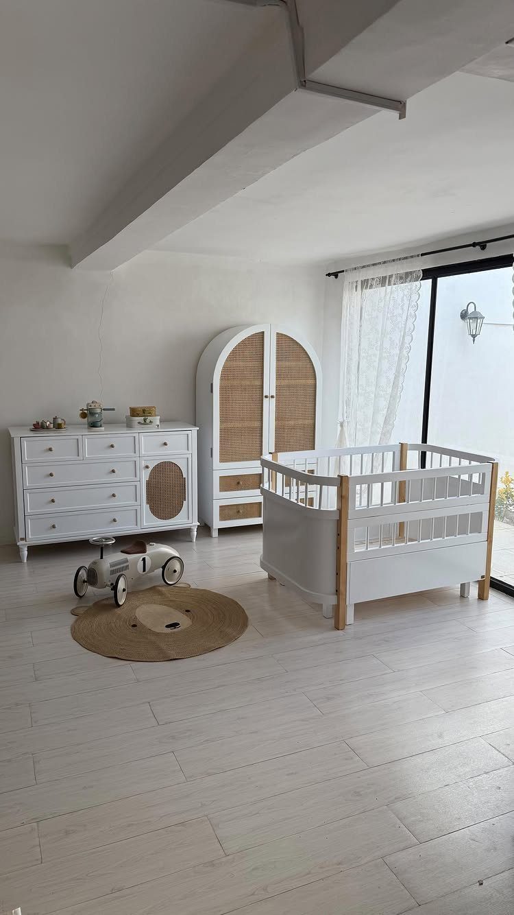 White nursery furniture including a crib, dresser, and wardrobe in a bright room.