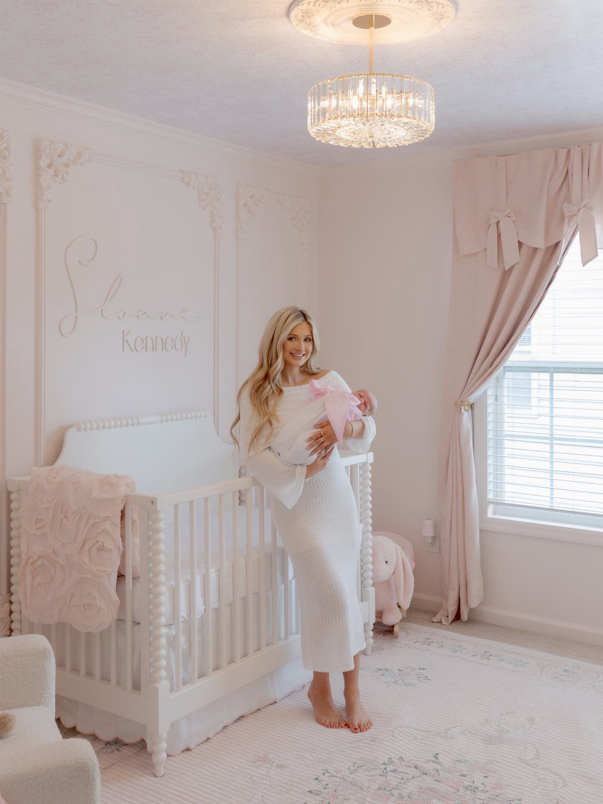 Woman standing in a pink nursery with a cursive name sign on the wall.