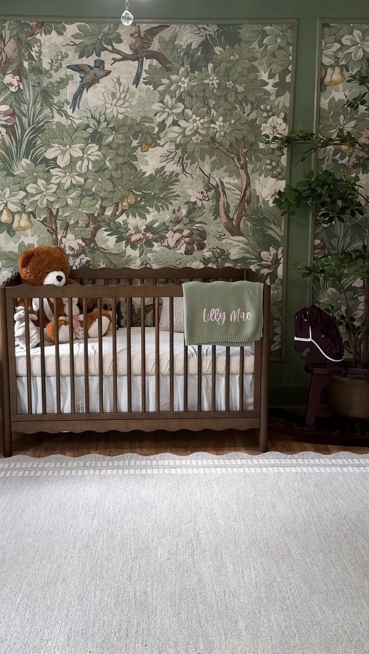 Wooden baby crib against a wall with green botanical bird wallpaper and white rug
