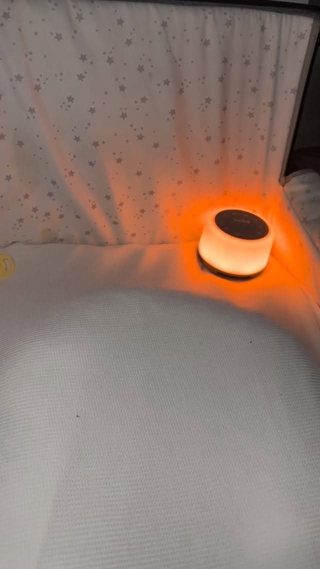 Small white sound machine glowing orange on a white surface near a crib.