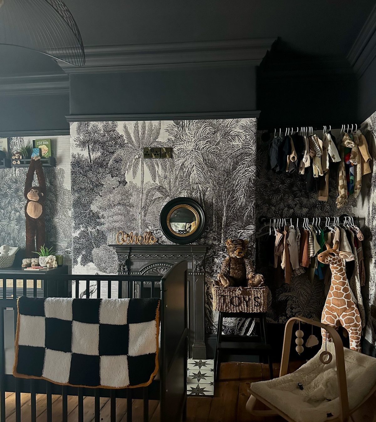 Nursery with black furniture, dark grey walls, and black and white tropical wallpaper.