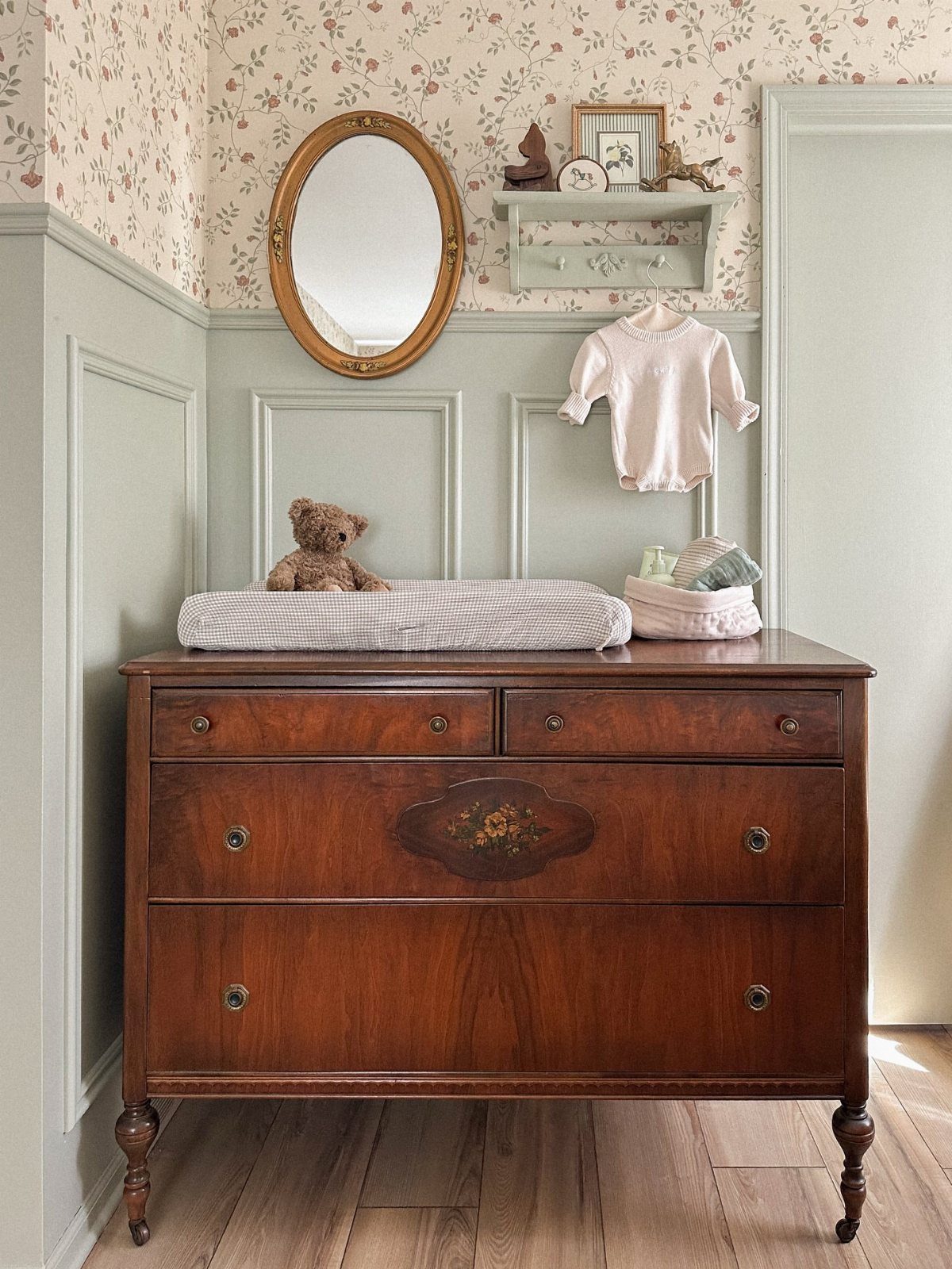 Dark wood dresser in a nursery with light green walls and floral wallpaper.