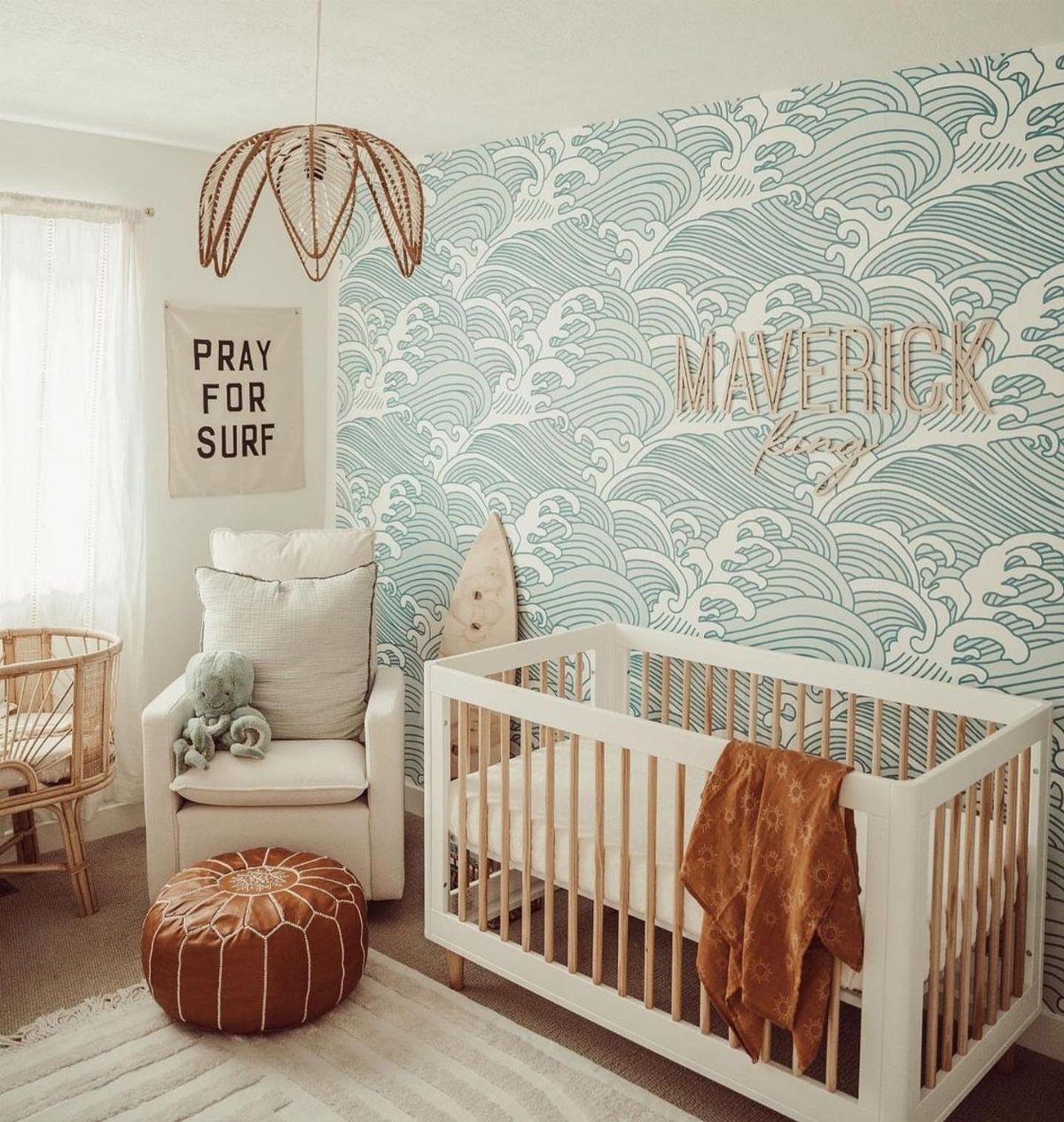 Nursery with blue wave wallpaper, white crib, and white armchair with leather pouf.
