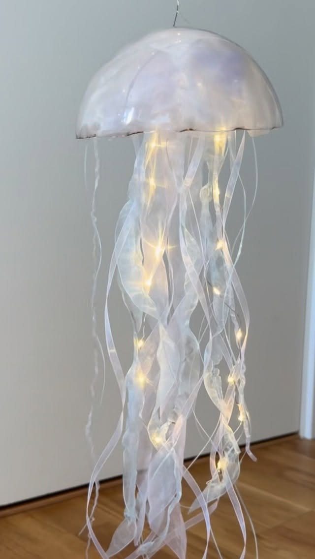 Hanging jellyfish decoration with translucent dome, flowing white ribbons, and warm fairy lights.