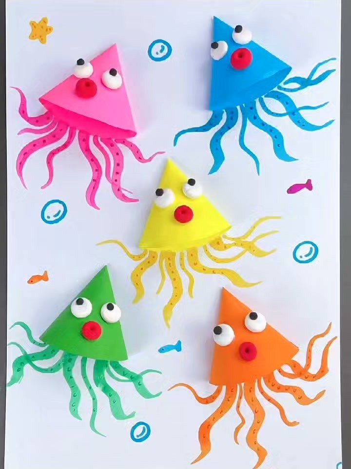 Colorful paper craft jellyfish with googly eyes and wavy tentacles on white paper.