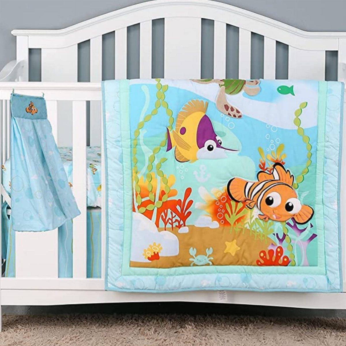 White baby crib with blue bedding and a colorful cartoon fish quilt.