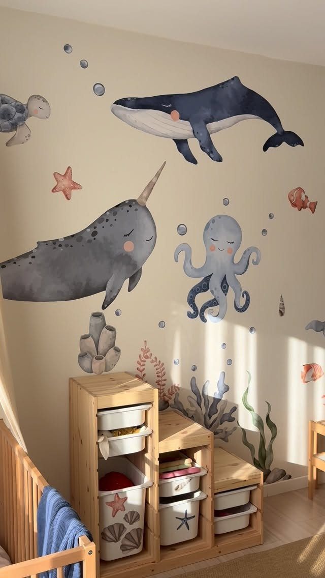 Watercolor ocean animal wall decals on a beige nursery wall above wooden storage bins