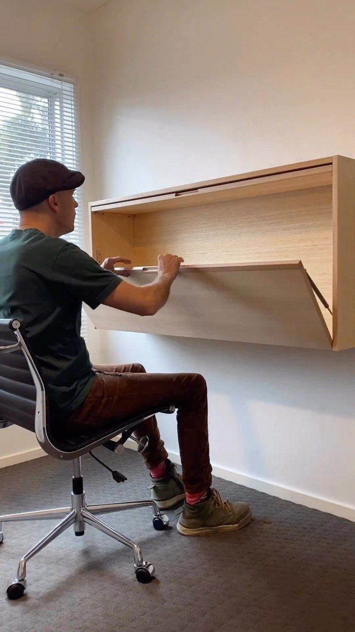 Man sitting at a light wood fold-down wall desk in a bright room.