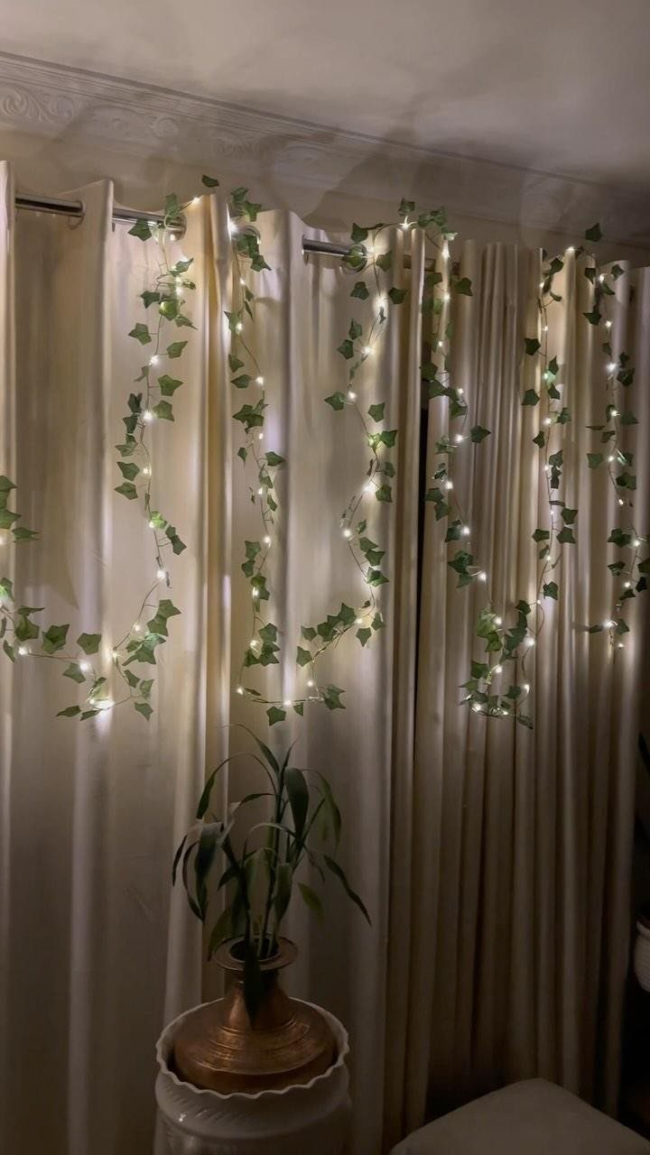 White curtains adorned with hanging ivy vines and twinkling fairy lights in a room.