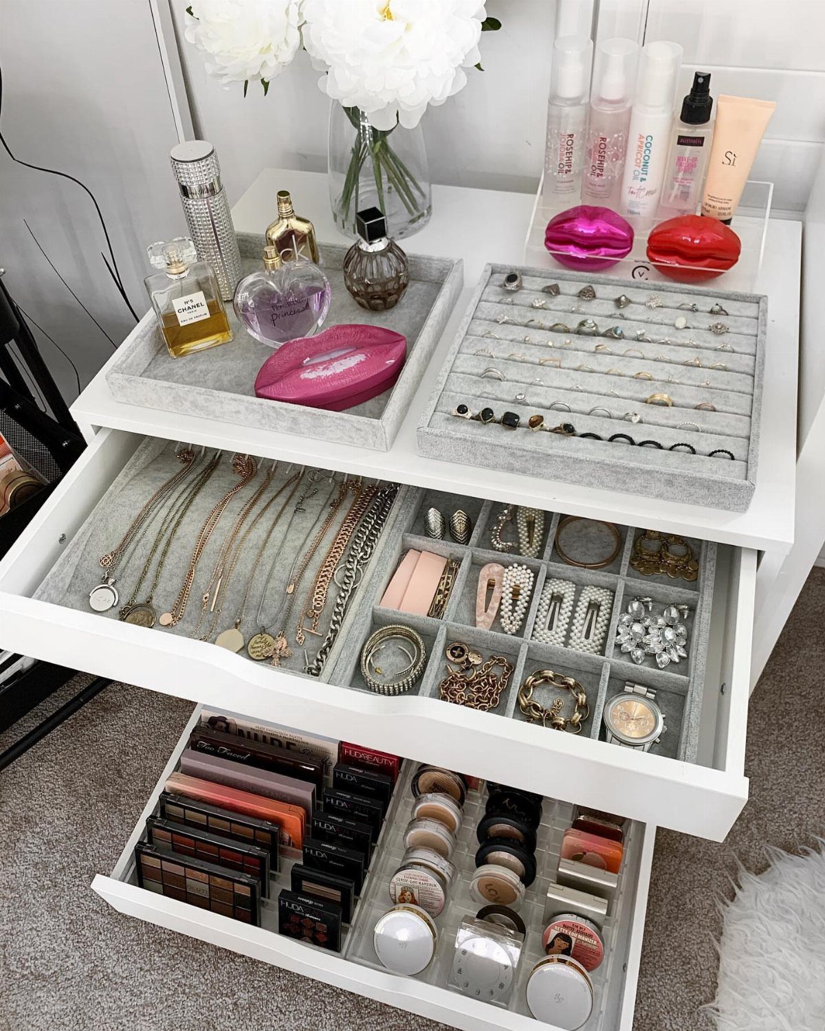 Jewelry and makeup organized in grey velvet trays inside white dresser drawers.