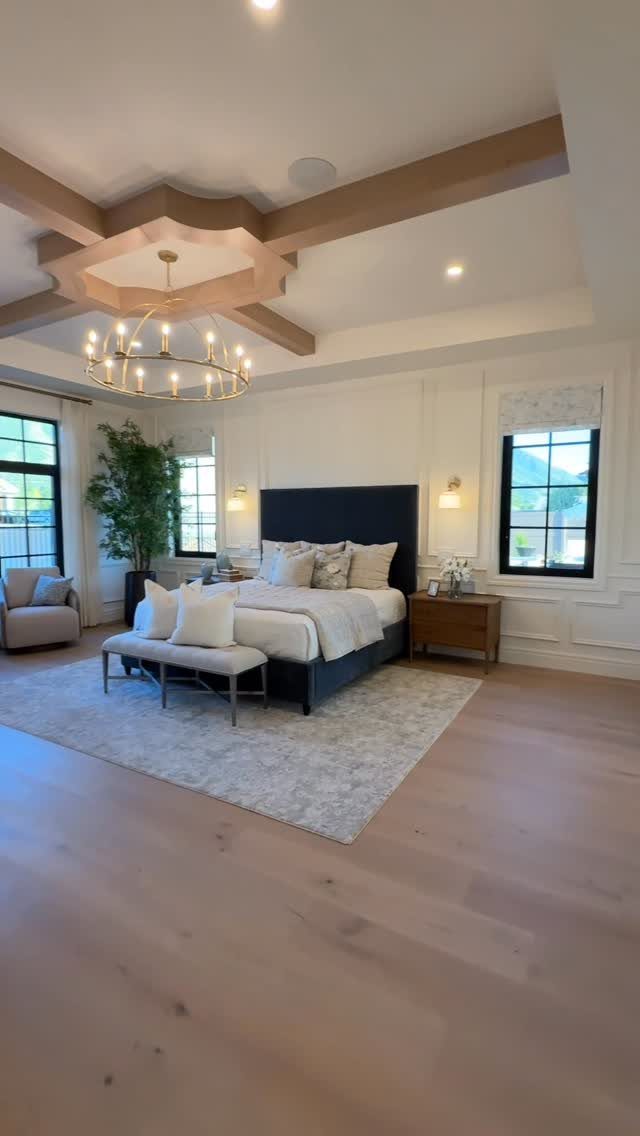 Master bedroom with a blue bed, coffered ceiling, and gold chandelier on wooden floors.