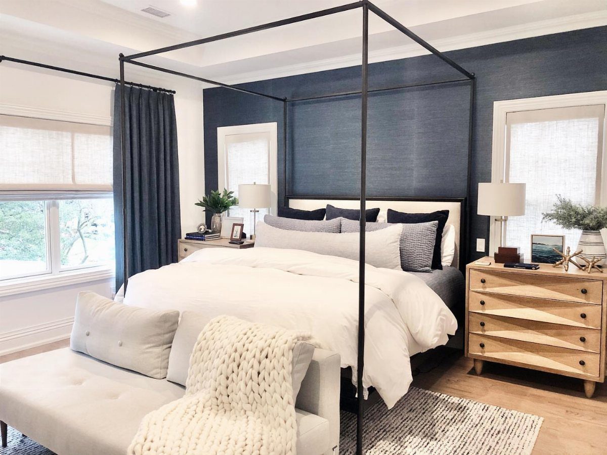 Canopy bed in a master bedroom with navy blue walls and wooden furniture.