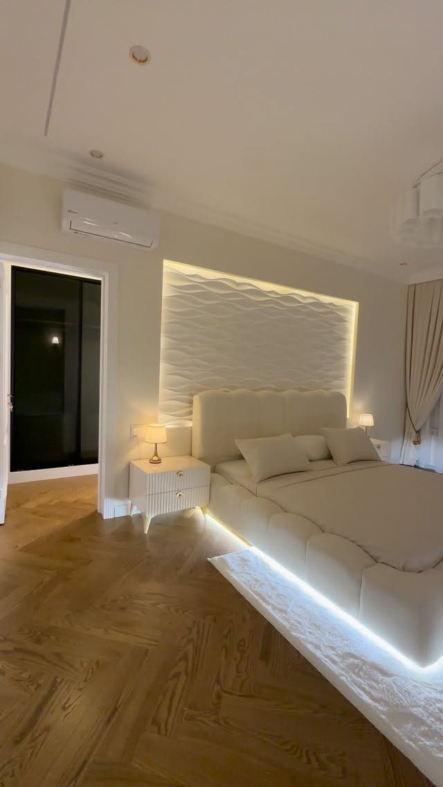 Modern master bedroom with a backlit textured wall and herringbone wood floors.