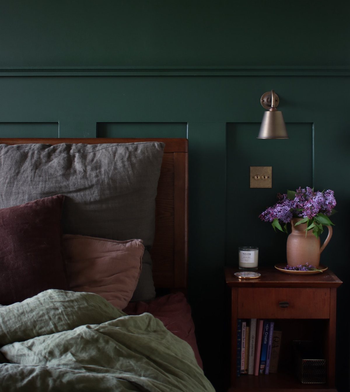 Deep green paneled bedroom wall with dusty rose and sage green linen bedding.