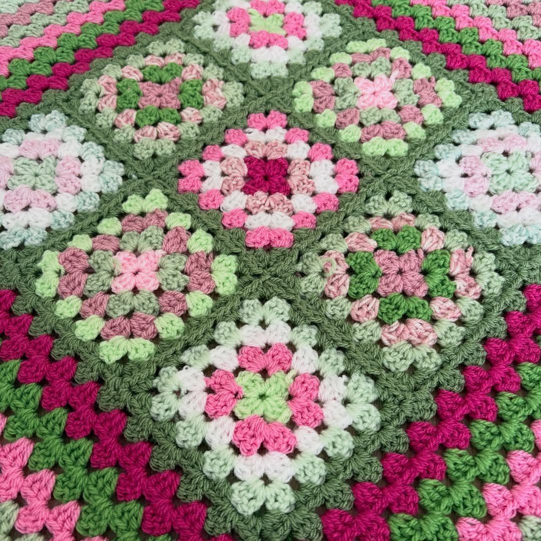 Crocheted granny square blanket with pink, green, and white floral patterns.
