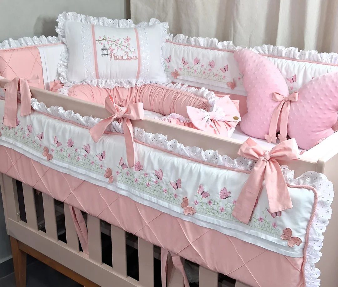 Pink and white crib bedding with butterfly embroidery and decorative ribbons in a nursery.