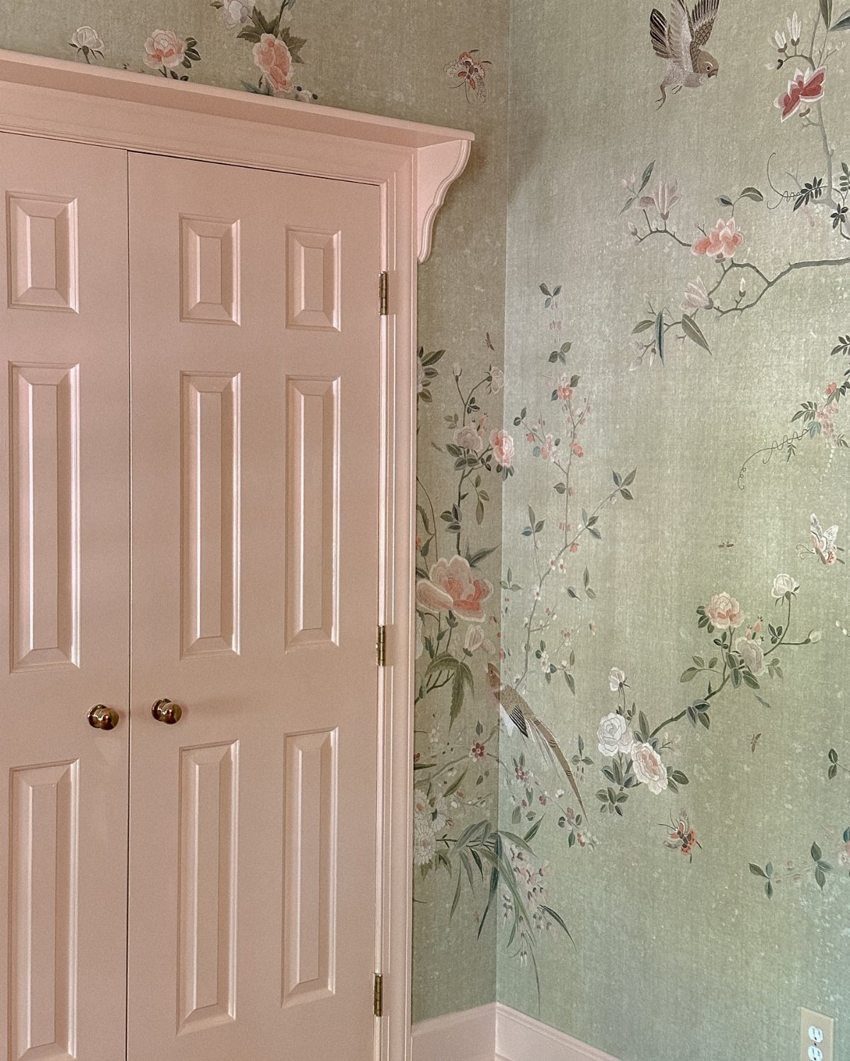 Floral wallpaper with pink blossoms and birds next to pale pink double doors.