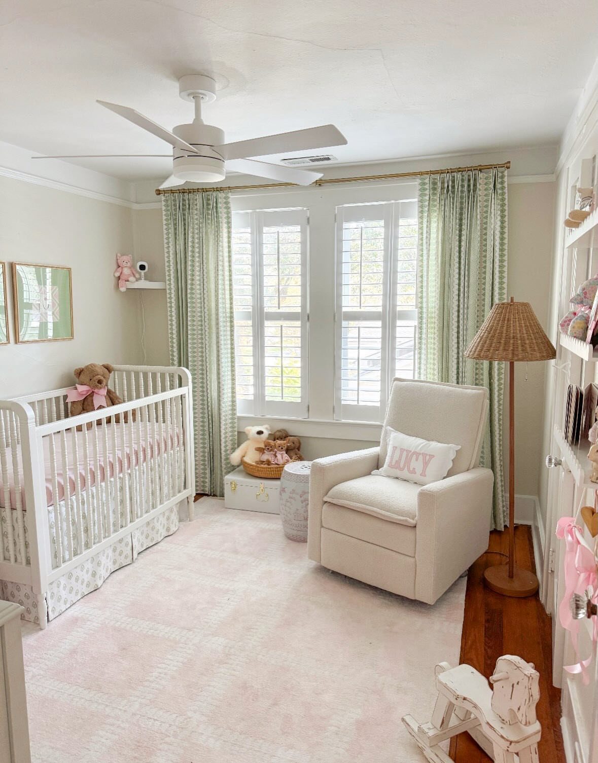 Nursery room with white crib, pink rug, and green patterned curtains.