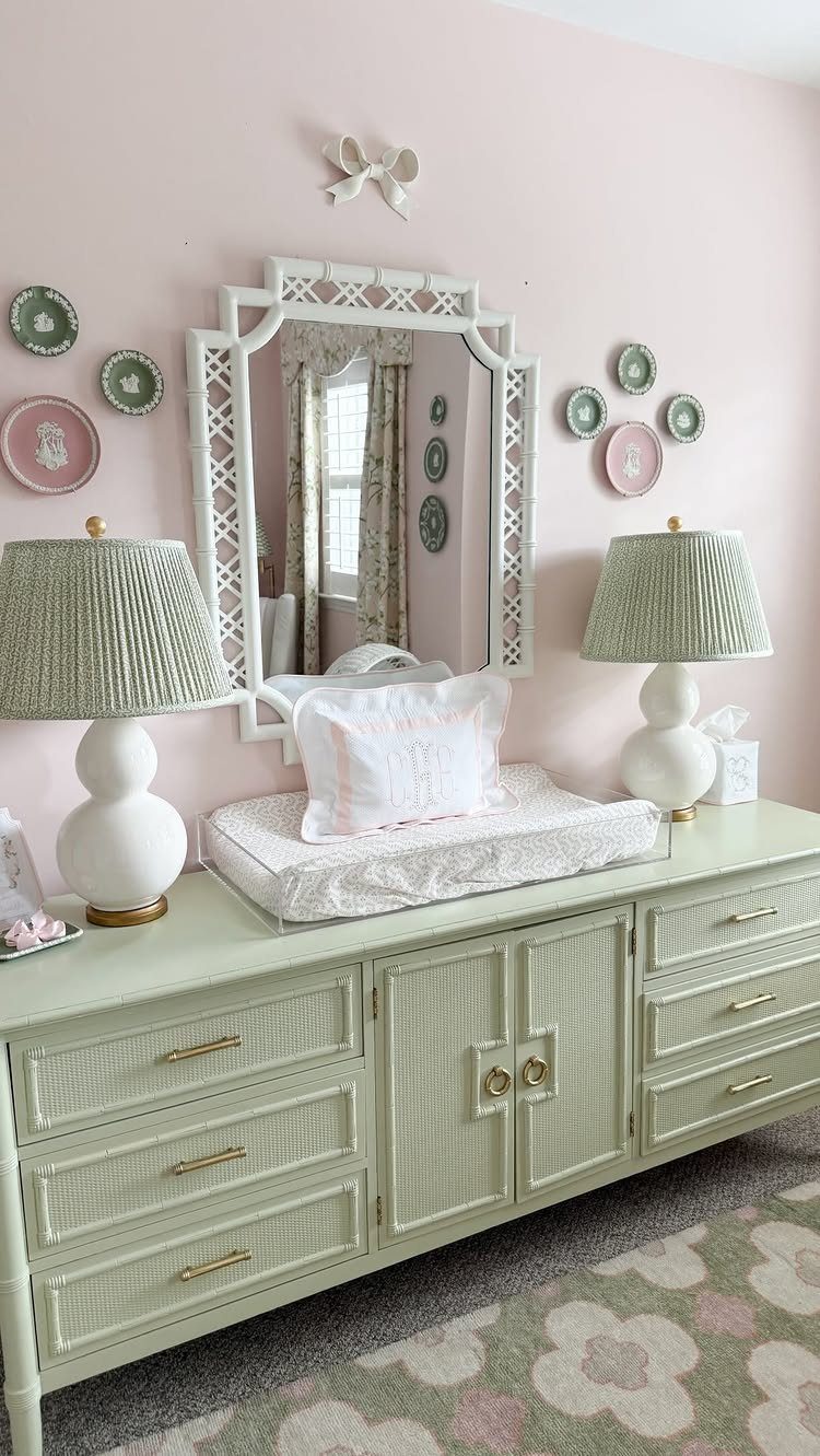 Light green dresser with changing pad and lamps against a pink nursery wall