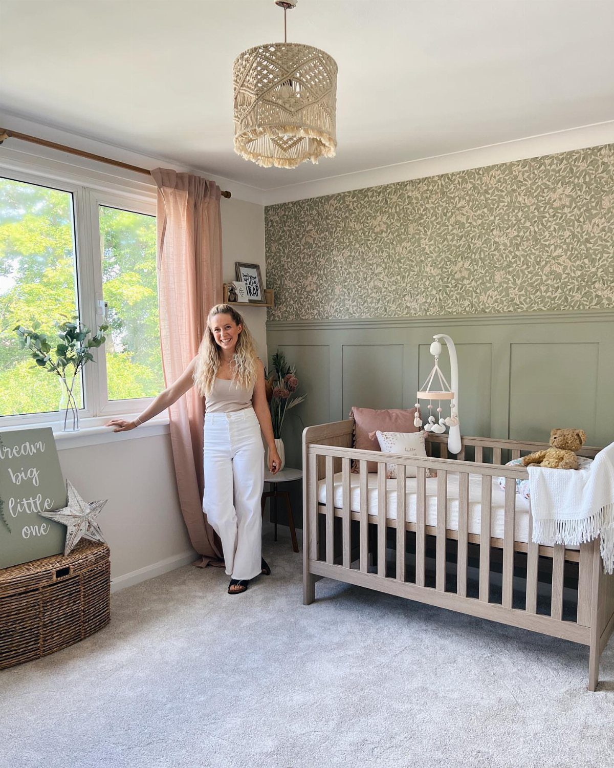 Woman standing in a nursery with sage green walls and floral wallpaper.