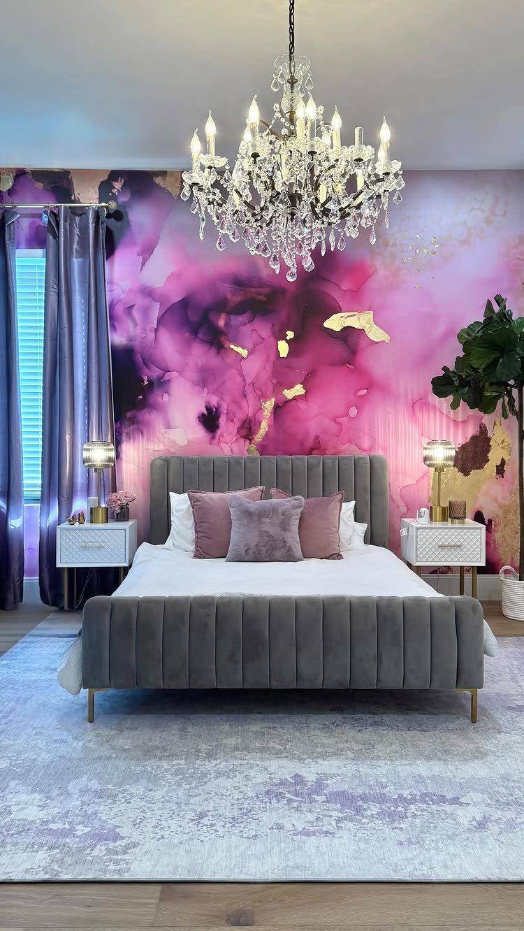 Grey velvet bed in a bedroom with pink and purple abstract wall mural.