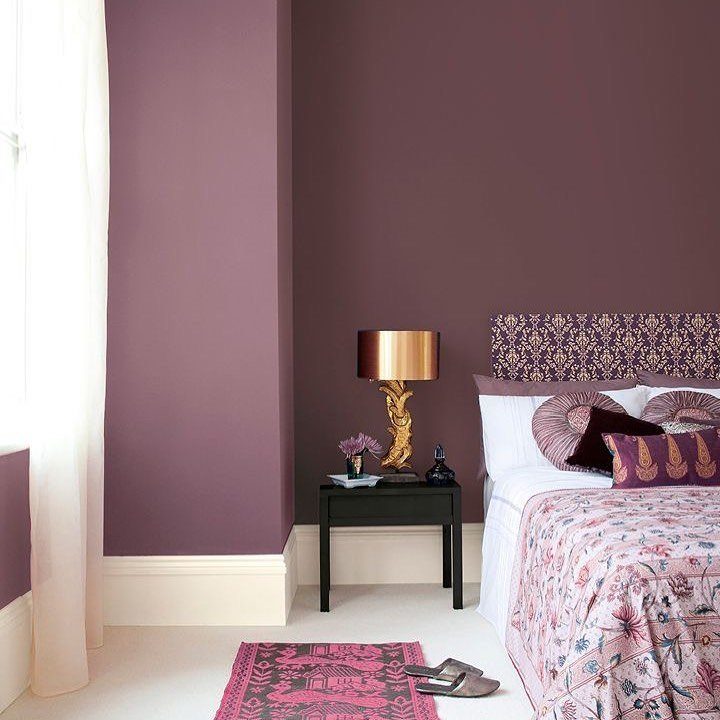 Plum walls and pink patterned bedding in a modern bedroom with gold lamp.