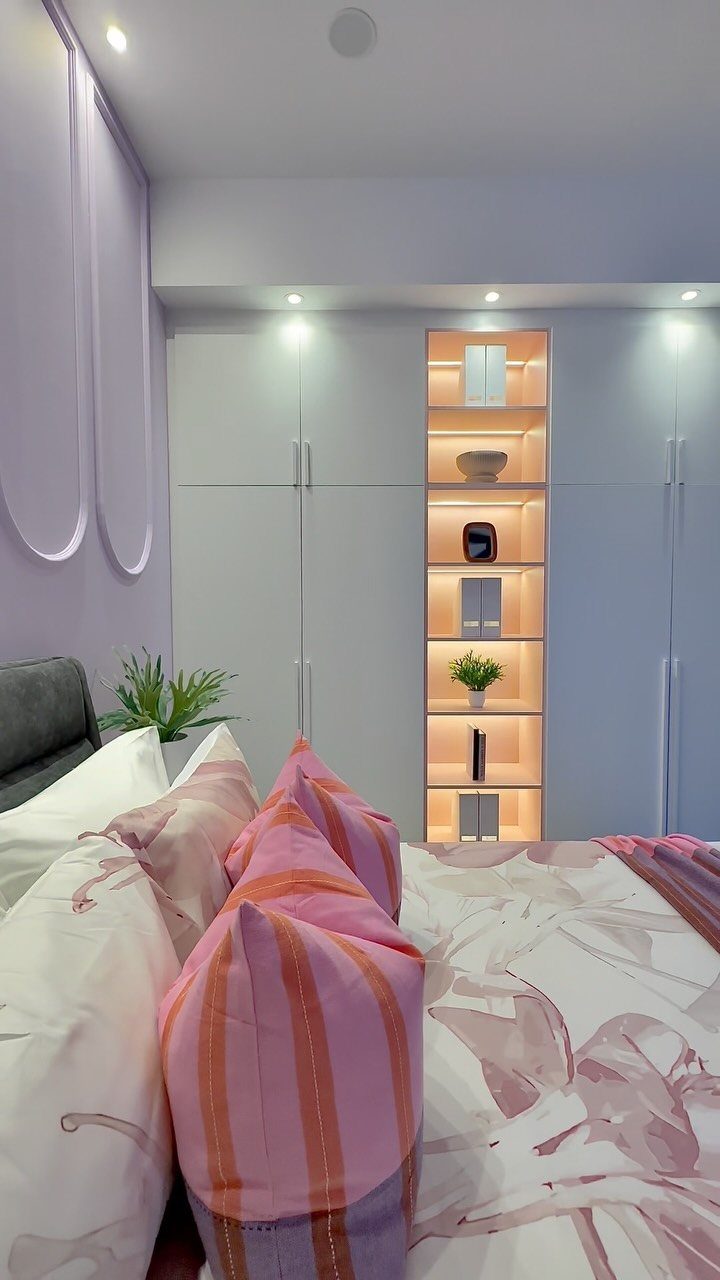 Bedroom with light purple walls, pink patterned bedding, and illuminated wardrobe shelving.