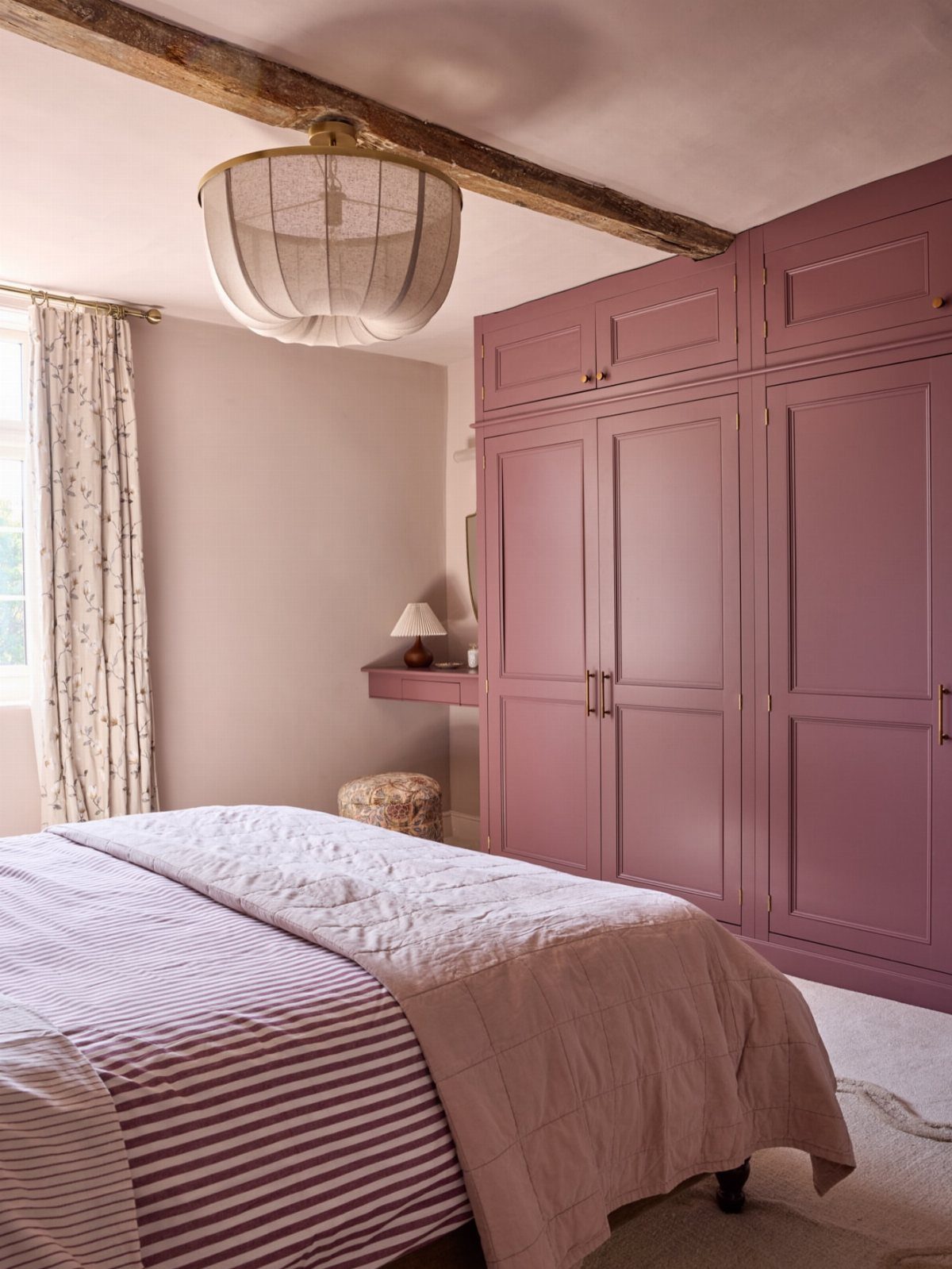 Bedroom with pale pink walls, mauve-purple built-in wardrobes, and pink and purple bedding.