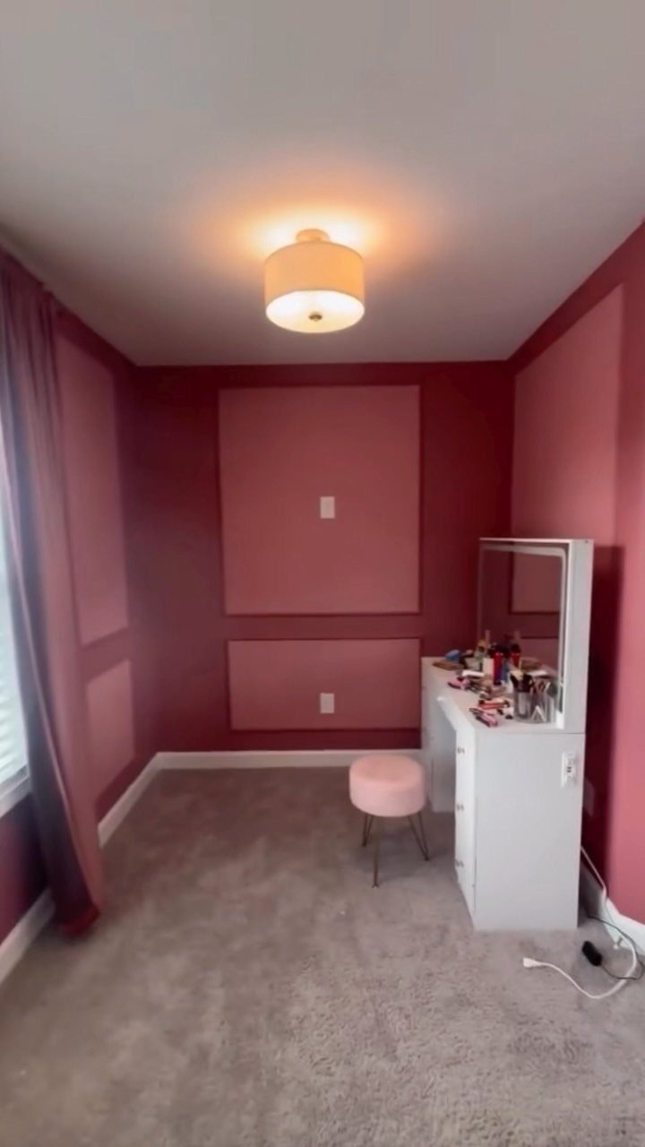 Dusty rose pink bedroom walls with a white vanity and purple curtains.