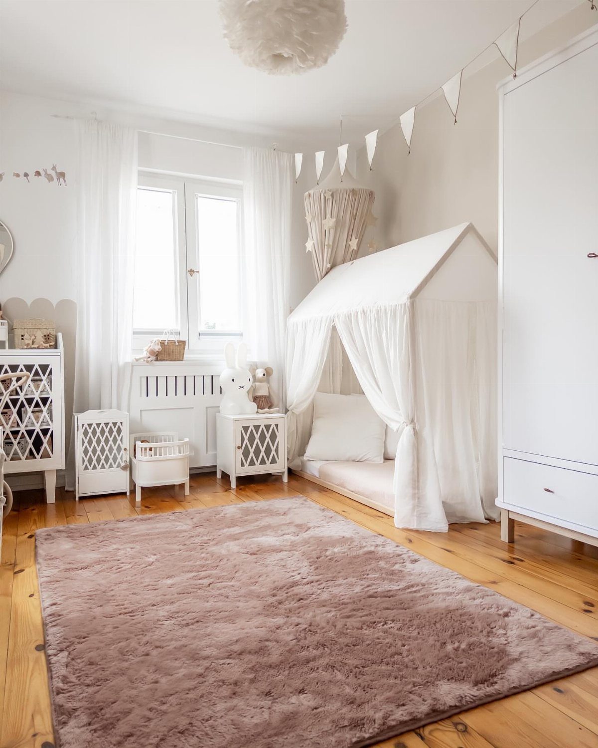 Mauve plush rug in a white nursery with a house-shaped bed canopy.