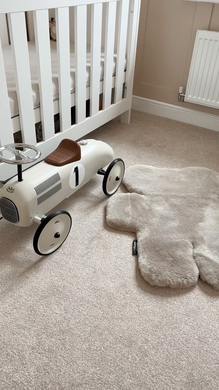 Small beige faux-fur rug placed on carpet next to a toy car and crib.