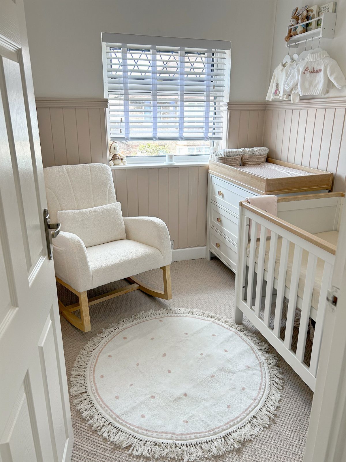 Round white fringed rug placed in a neutral nursery with a rocking chair.